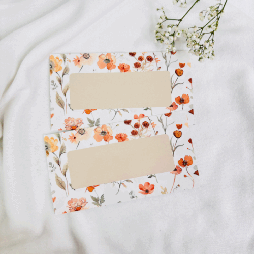 Dwie beżowe karty kategorii z kwiatowym motywem w odcieniach pomarańczu i beżu, leżące na białym tle obok białych kwiatów.