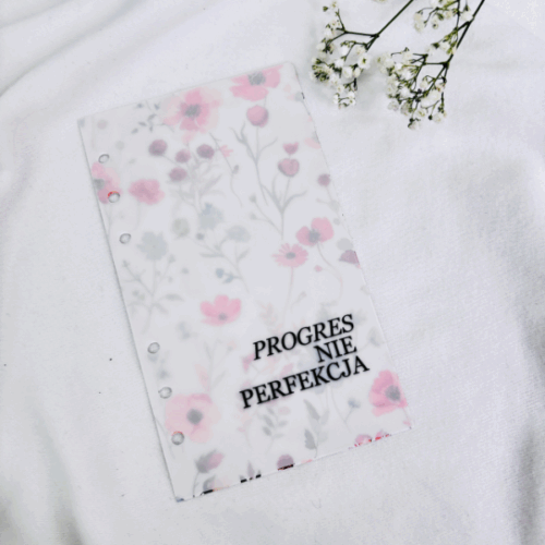 Okładka do segregatora z napisem „PROGRES NIE PERFEKCJA” i delikatnym wzorem kwiatów w ciepłych odcieniach na białym tle.