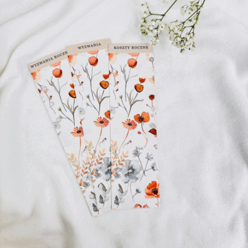 Trzy beżowe zakładki do segregatora z napisami: Wyzwania, Wyzwania Roczne, Koszty Roczne. Zakładki ozdobione są delikatnym kwiatowym wzorem w odcieniach pomarańczu i beżu.